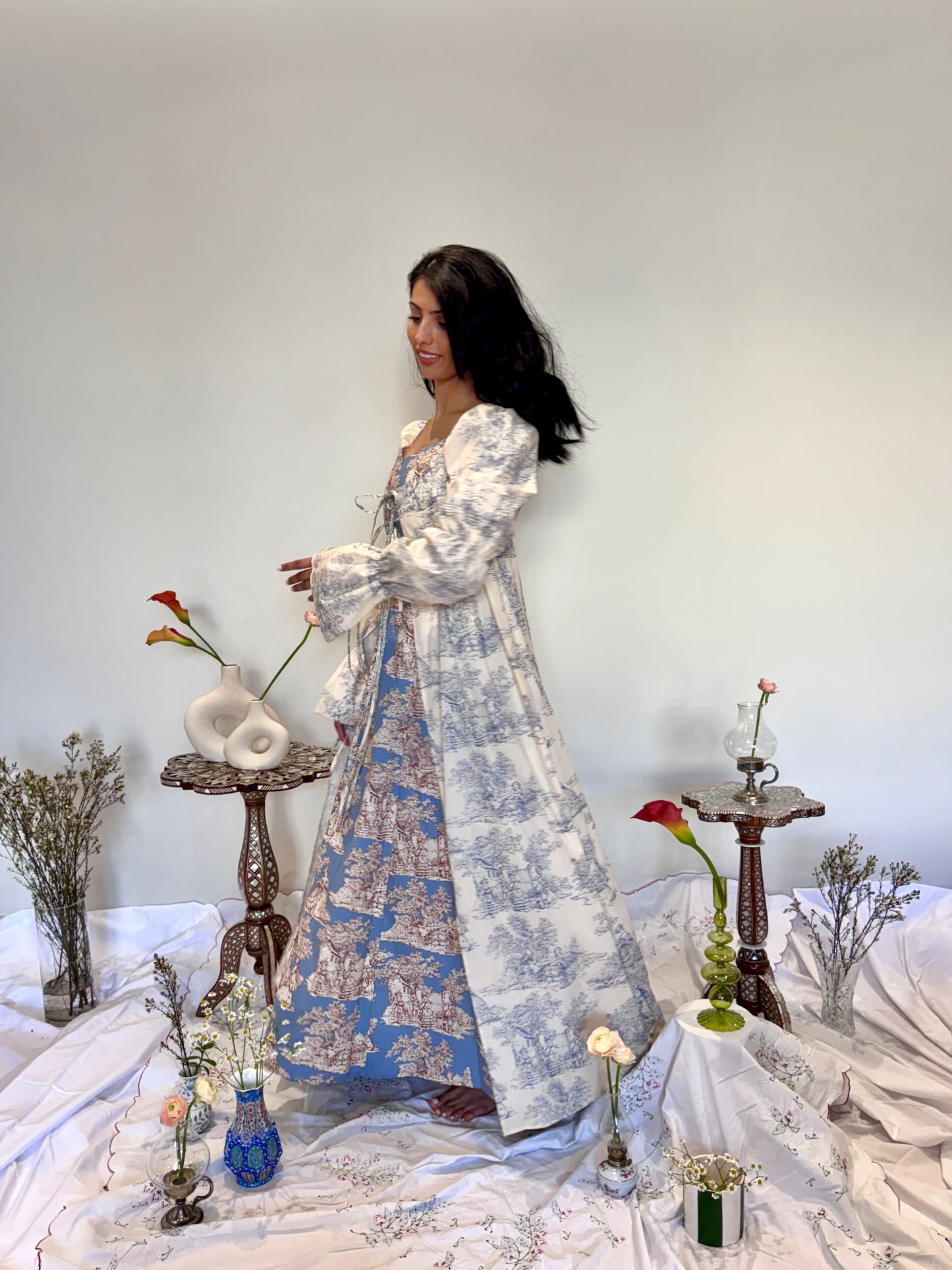 Woman in a floral dress standing in a room with decorative elements and flowers.